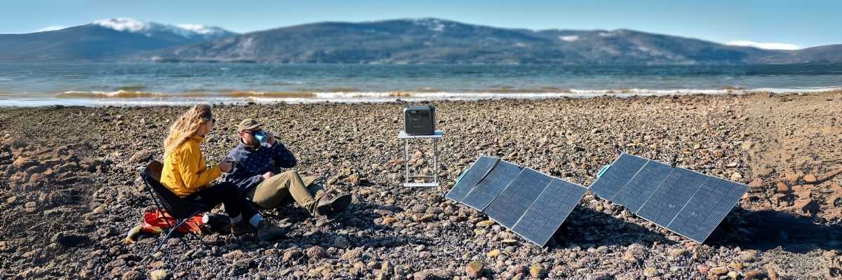 Portable power station solar charging at a lakeside camping site with two people enjoying the outdoors
