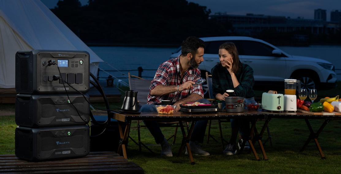 A couple using a portable power station to power cooking appliances while camping, demonstrating its convenience for off-grid energy needs.