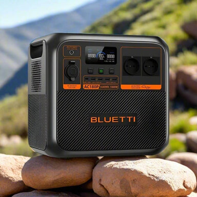Bluetti AC180P portable power station sitting on rocks with scenic mountain background and natural sunlight