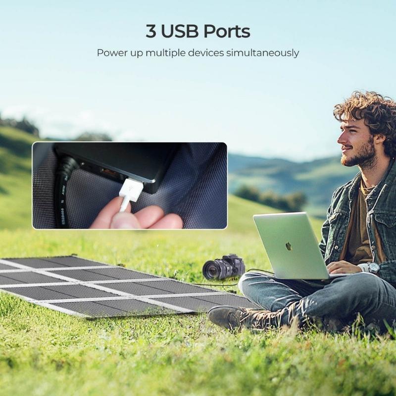Renogy 200W solar blanket charging laptop and camera through three USB ports in grassy outdoor setting