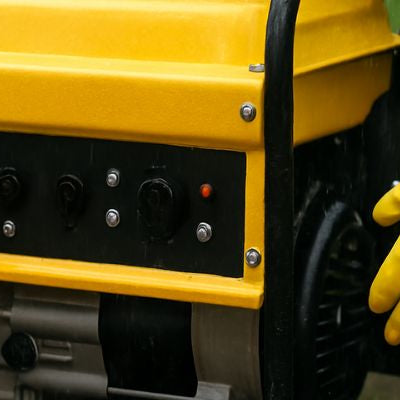 Portable yellow generator in the rain with people wearing gloves plugging it in on wet pavement.