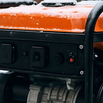 Portable generator with orange fuel tank outdoors in snowy winter setting.