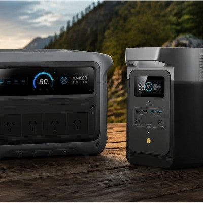 Anker Solix and EcoFlow power stations on a wooden deck by a lakeside at sunset, with a tent and camping setup in the background