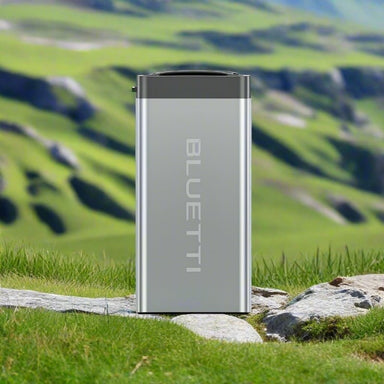 Bluetti B70 modular battery standing outdoors on rocky grass.