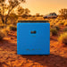 Bluetti RV5 power hub standing on cracked red outback earth at golden hour, a dusty 4WD blurred in the distance