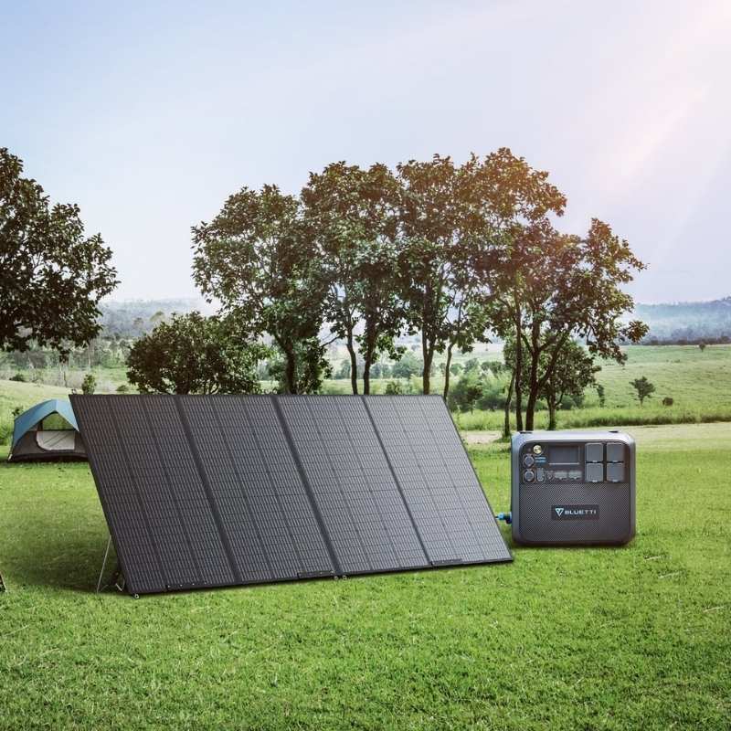 A foldable solar panel and Bluetti generator set up on grassy field with trees and a tent in the background