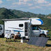 Man seated beside a caravan and fold-out table with portable solar panels and a power station.