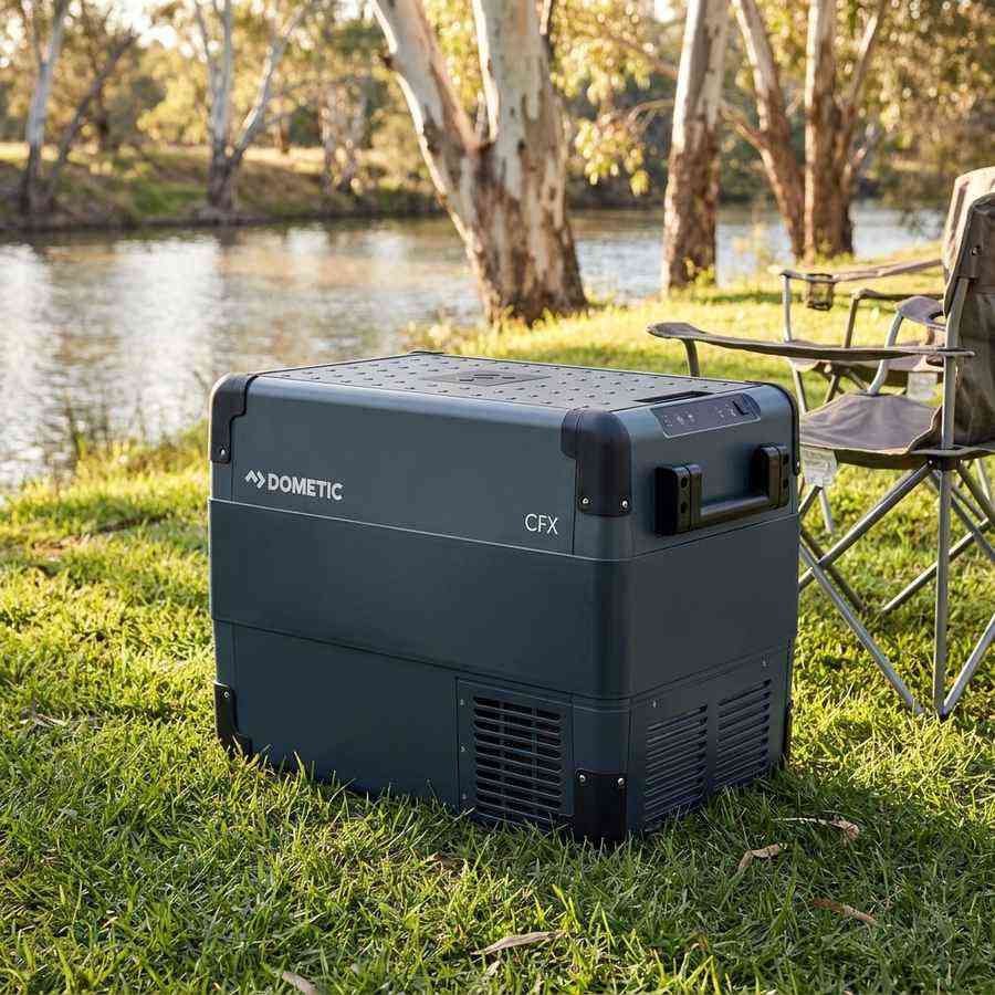 Dometic CFX2 45 portable fridge freezer on the grass beside camp chairs at a riverside campsite
