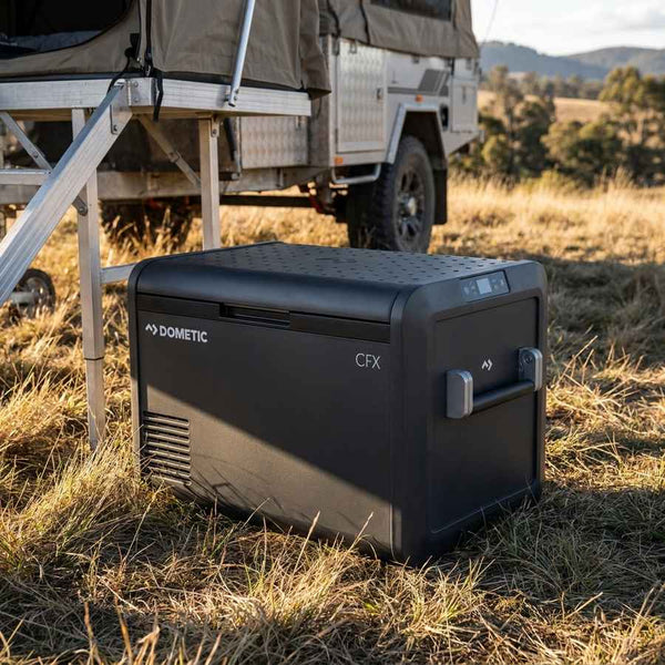 Dometic CFX5 55 portable fridge freezer on the grass beside a camper trailer awning in the high country