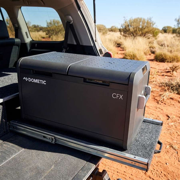 Dometic CFX5 75DZ dual zone portable fridge freezer on a pull-out fridge slide in a 4WD wagon, outback red dirt behind