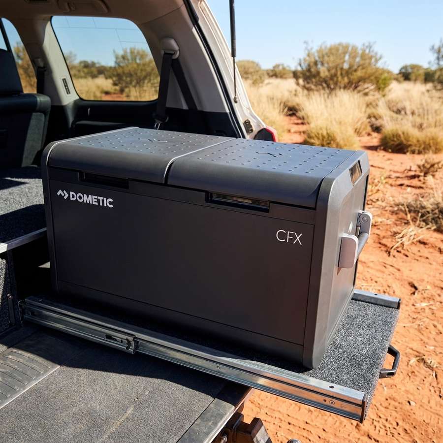 Dometic CFX5 75DZ dual zone portable fridge freezer on a pull-out fridge slide in a 4WD wagon, outback red dirt behind