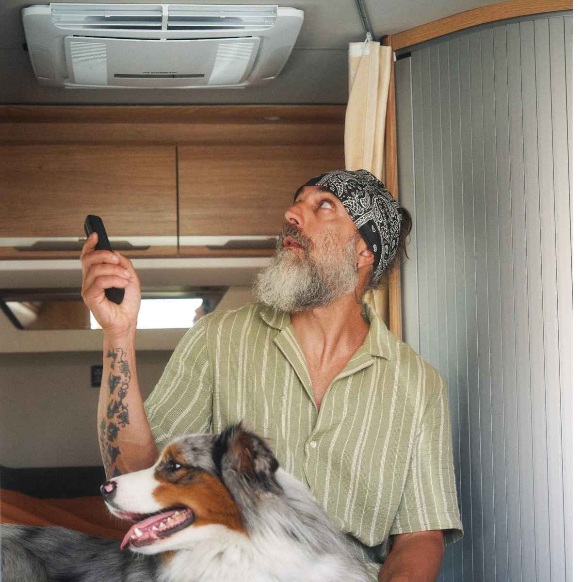 Man with two dogs inside a motorhome using the remote for a Dometic air distribution box in the ceiling above