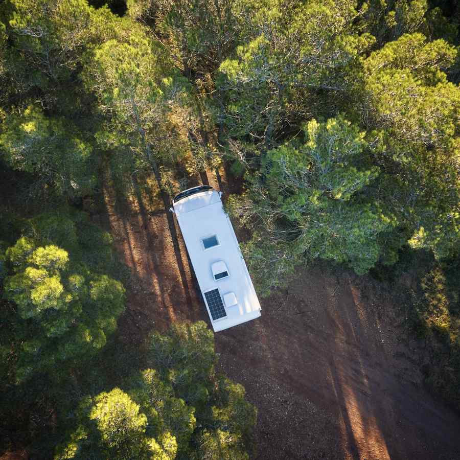 Overhead view of a caravan on a red dirt track through bush with a Dometic rooftop air conditioner and solar panel on the roof