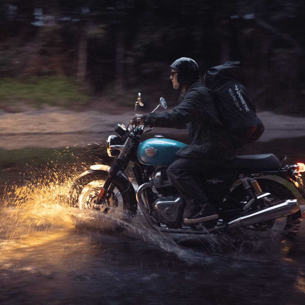 Rider on a motorcycle through a wet forest track with a Dometic Pico carry bag strapped on the back