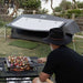Dometic Pico FTC 2x2 TC-I pitched with the awning up at a coastal campsite while a bloke cooks skewers nearby