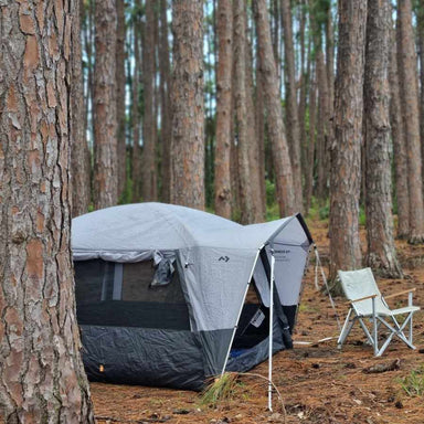 Dometic Reunion FTG 4x4 Redux pitched among pine trees with the front canopy up and a camp chair alongside