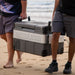 Two men carrying MyCOOLMAN 53L fridge freezer across sandy beach
