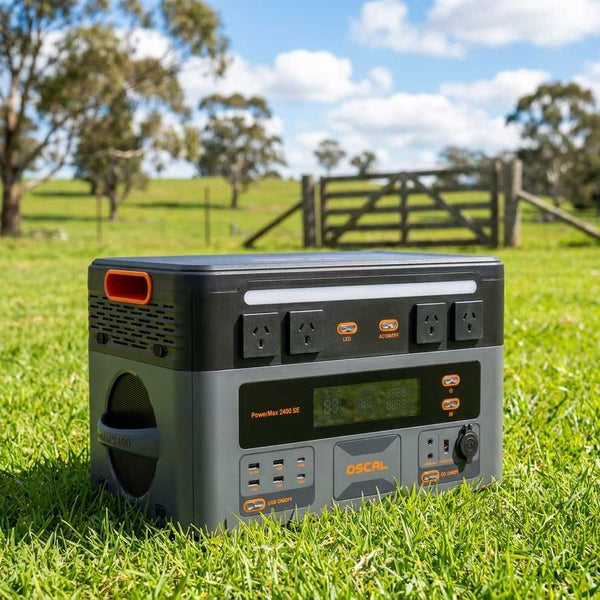 OSCAL PowerMax 2400SE power station sitting on green grass in front of a timber farm gate