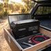 Renogy 12V 200Ah battery mid-install in an open battery box in a 4WD canopy drawer, tailgate open to a bush track