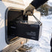 Gloved hand carrying the Renogy Pro 200Ah battery by its rope handle from a frosted caravan storage locker
