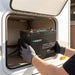 Hands lifting the Renogy Core Mini 100Ah battery out of an open caravan storage locker
