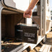Renogy Core Mini 200Ah battery held by its rope handle beside an open caravan storage locker