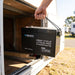 Renogy Core Mini 300Ah battery held by its rope handle beside an open caravan storage locker