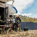 Father and son cooking outside a caravan using a BBQ and solar-powered portable battery.