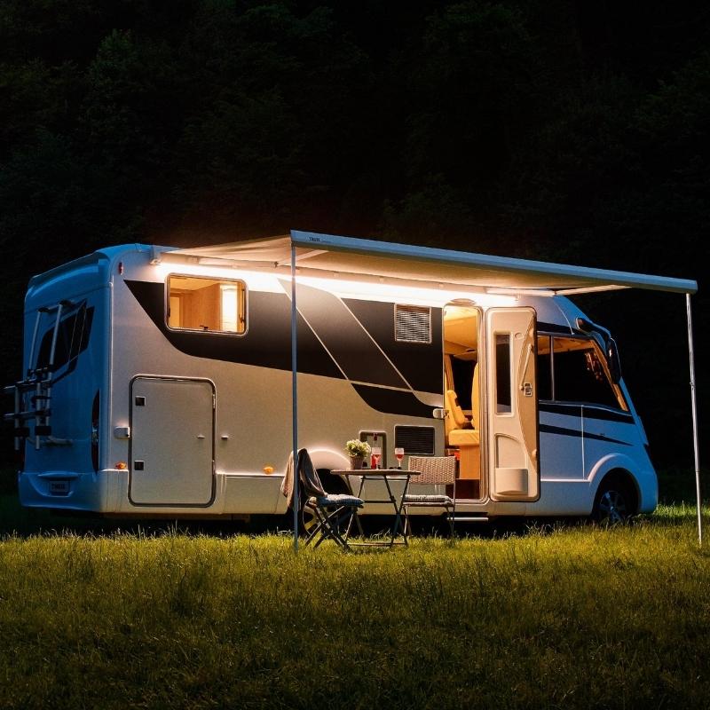 The Thule 5200 manual awning extended during the night, providing shelter and illumination in a camping setup.