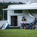 A couple relaxing under the Thule Omnistor 5200 Electric 12V awning on a camper van, ideal for outdoor adventures.