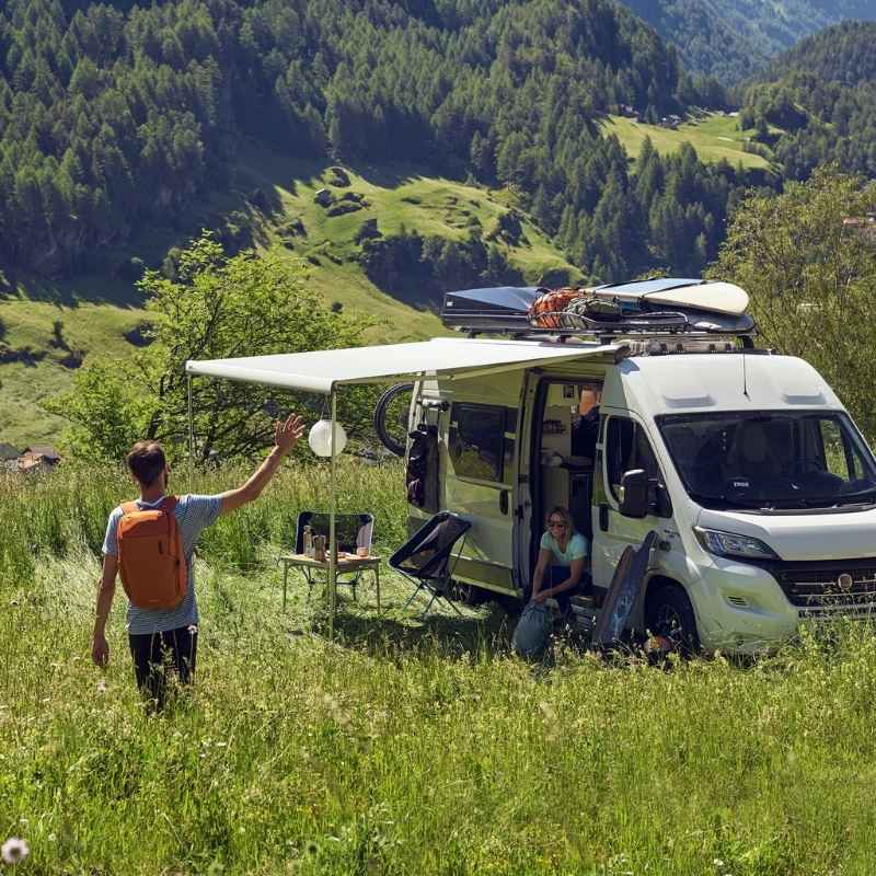 Thule Omnistor 6300 Awning extended over a camper van in the mountains, with outdoor gear and camping essentials, demonstrating the awning's versatility.