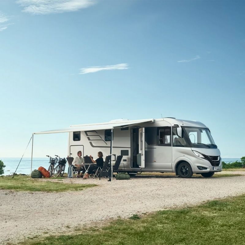 The Thule Omnistor 8000 Electric 230V Awning providing shade for relaxation, with chairs and a table set up outside the RV.